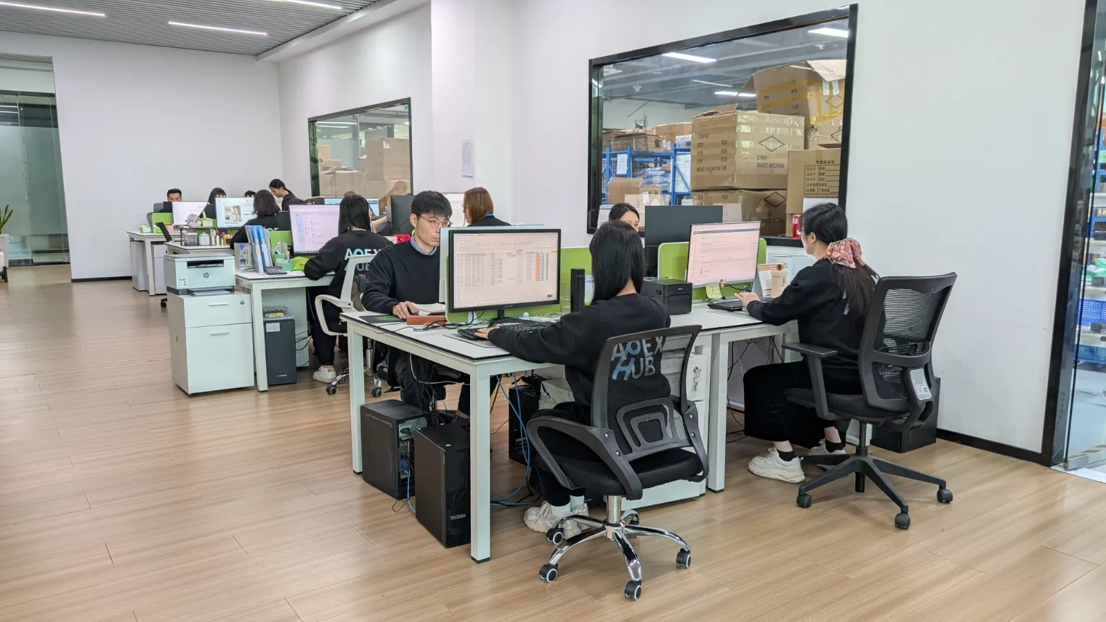 Apex Hub team at work in the Shenzhen office, with the warehouse visible behind the glass